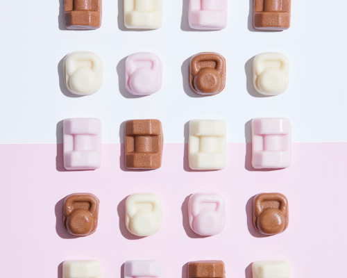 Colorful chocolate-shaped candies arranged in a grid on a light pink background